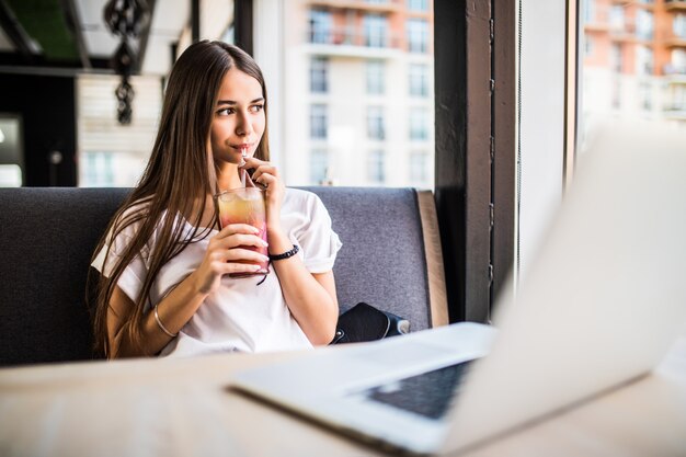 Gorgeous cheerful woman freelancer in a good mood, using laptop computer, sitting in cafes, sipping Mojitos.