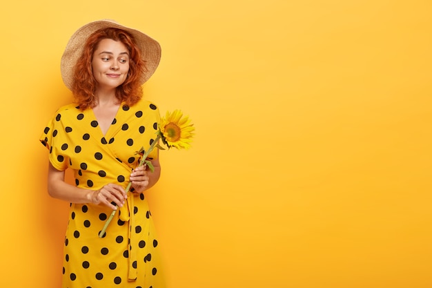 Free photo gorgeous redhead woman posing in yellow polka dress and straw hat