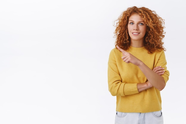 Free photo gorgeous smiling redhead woman with curly hair pointing at left