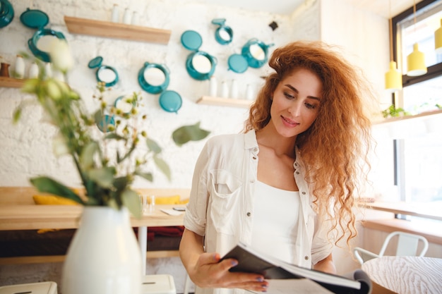 Free photo gorgeous smiling redhead young lady standing in cafe reading