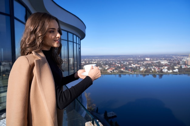 Free photo gorgeous woman drinking coffee while standing on balcony