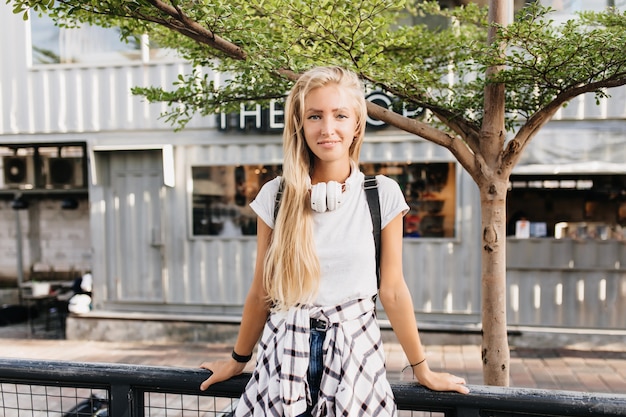 Gorgeous woman in white headphones standing on street background