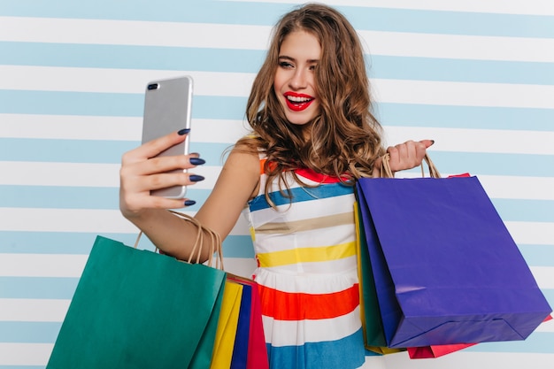 Free Photo gorgeous woman with red lips making selfie on striped wall. attractive female shopaholic taking picture of herself.