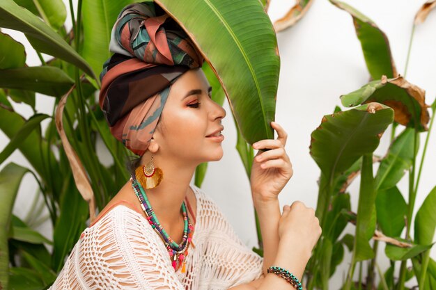 Gorgeous woman with turban on head, colorful earrings and boho necklace posing