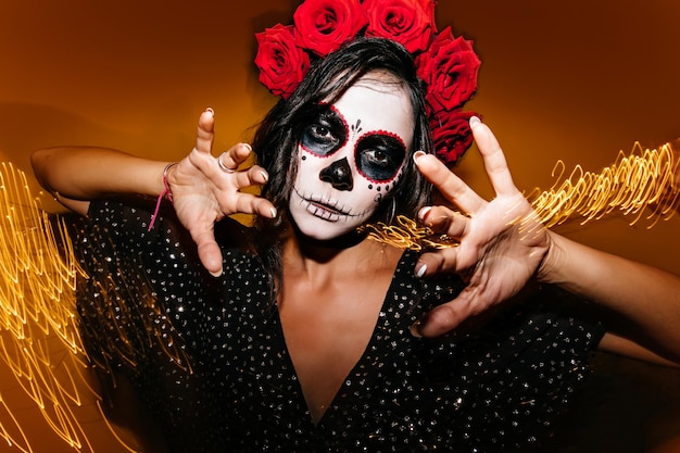 Free photo gorgeous young female model with white face painting posing in halloween studio photo of debonair zombie girl standing on sparkle background