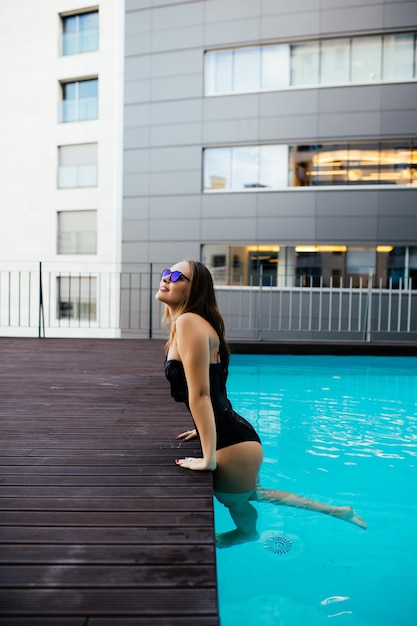 Free photo gorgeous young woman wears black sunglasses and black top swimming in the pool on age background of jungles and relaxes on resort, vacation, summer, luxury lifestyle