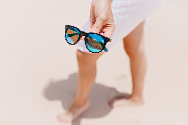 Graceful barefooted lady posing with sunglasses. Outdoor portrait of woman with tanned legs with sparkle glasses on foreground.