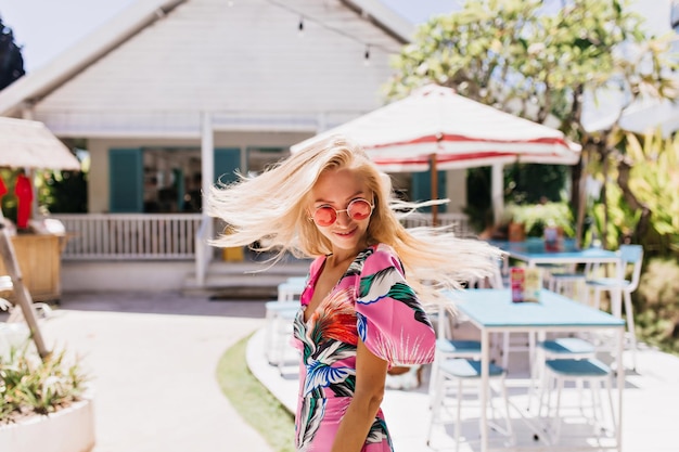 Free Photo graceful blonde woman with tanned skin posing near outdoor cafe portrait of fascinating fairhaired lady in summer dress dancing at resort