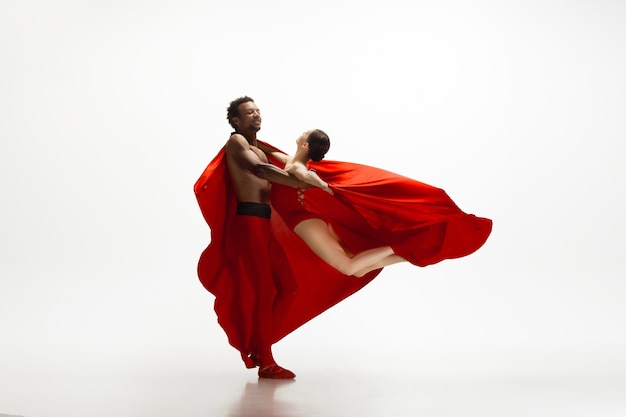 Graceful classic ballet dancers dancing isolated on white studio background. Couple in bright red clothes like a combination of wine and milk. The grace, artist, movement, action and motion concept.