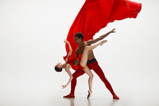 Free photo graceful classic ballet dancers dancing isolated on white studio background. couple in bright red clothes like a combination of wine and milk. the grace, artist, movement, action and motion concept.