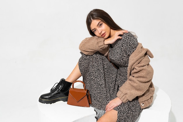 Graceful european woman in winter fur coat and stylish dress sitting. Wearing ankle boot in black leather.