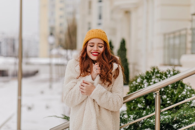 Free photo graceful ginger young woman posing in winter. inspired caucasian girl in stylish coat standing on the street with smile.