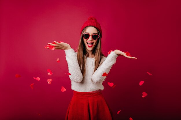 Graceful girl in fluffy sweater throwing out heart confetti