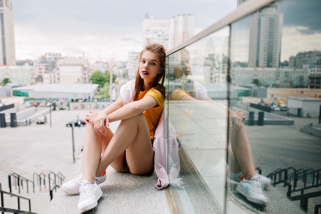 Free photo graceful girl with serious face expression waiting friend on parapet enjoying amazing city view