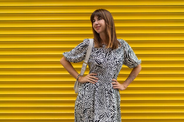 Graceful woman with tatoo on hand posing over yellow  urban wall.