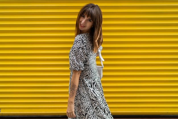 Graceful woman with tatoo on hand posing over yellow  urban wall.