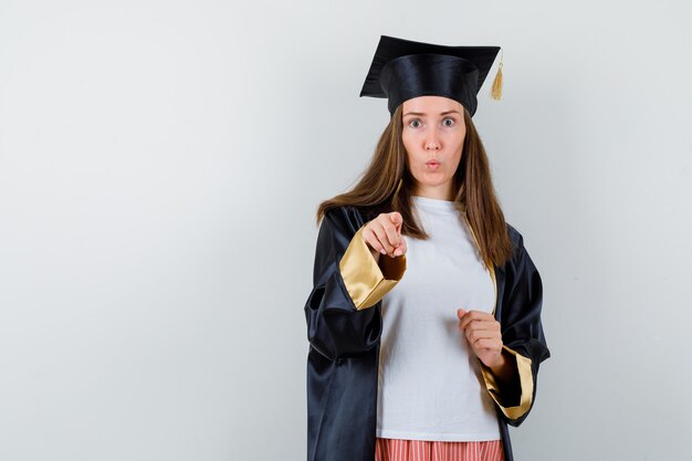 Graduate woman pointing at camera in casual clothes, uniform and looking bewildered. front view.