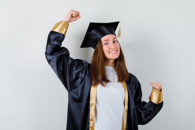 Graduate woman showing winner gesture in casual clothes, uniform and looking happy , front view.