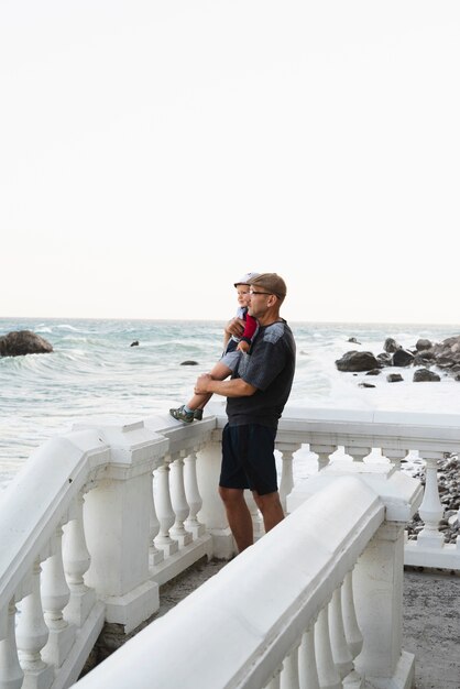 Grandfather holding grandson and looking at sea