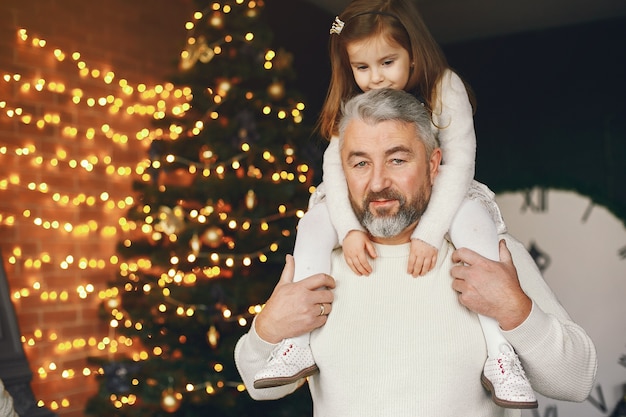 Free photo grandfather sitting with his granddaughter. celebrating christmas in a cozy house. man in a white knited sweater.