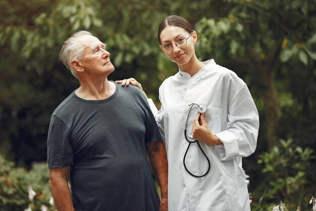 Grandfather with wheelchair assisted by nurse outdoor. Senior man  and young caregiver in the park.