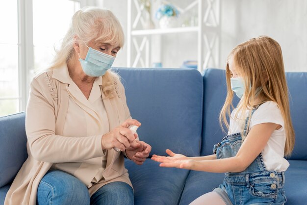 Grandma and girl with mask using hand sanitizer