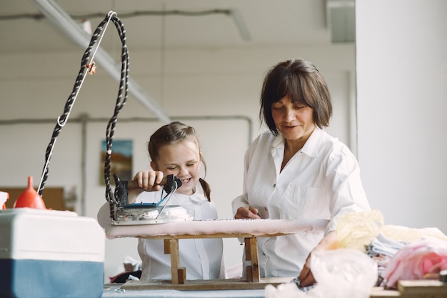 Grandma with little granddaughter iron clothes in the factory