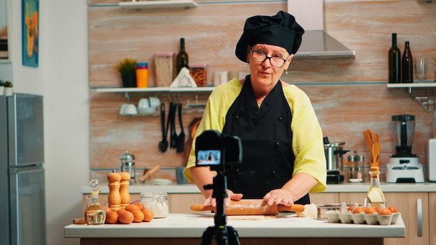 Free photo grandmother making cooking vlog, recording herself on camera. retired blogger chef influencer using internet technology communicating, shooting blogging on social media with digital equipment