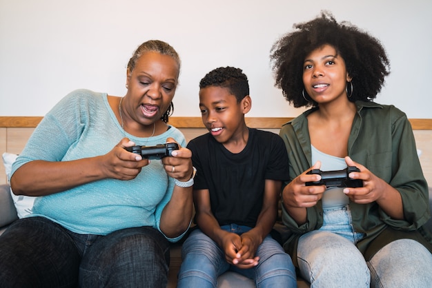 Grandmother, mother and son playing video games at home.