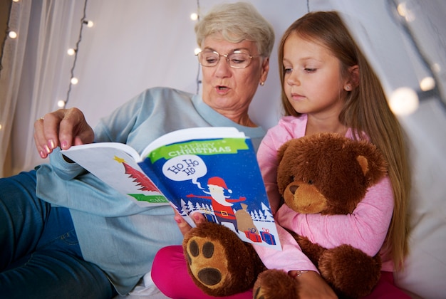 Free photo grandmother reading book out to her granddaughter