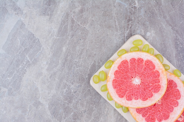 Free photo grapefruit slices and green grapes on wooden board.