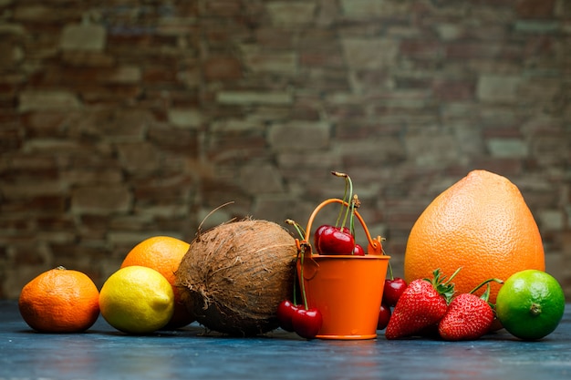 Free photo grapefruit with orange, lime, lemon, strawberry, cherry, tangerine, coconut side view on brick stone and blue background