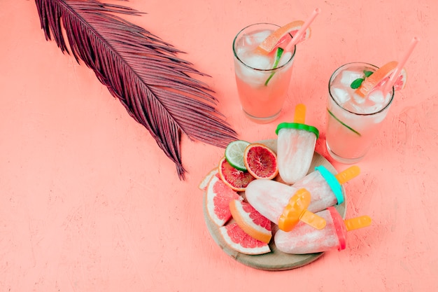 Grapefruits slices; juice and popsicles with leaf on coral textured background