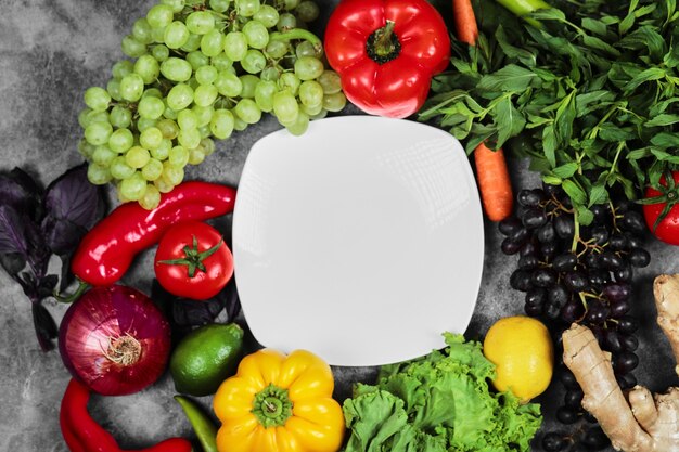 Grapes, peppers, greens, lemon, tomato , ginger and white plate on marble background. 