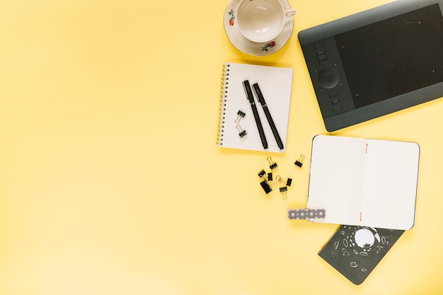 Graphic digital tablet and ceramic empty cup with stationeries on yellow background