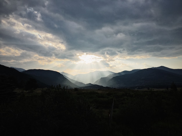 Free photo grassy field with plants with mountains and the sun shining through the clouds in the background