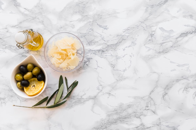 Free Photo grated cheese with olive and lemon slice bowl and oil bottle on white backdrop