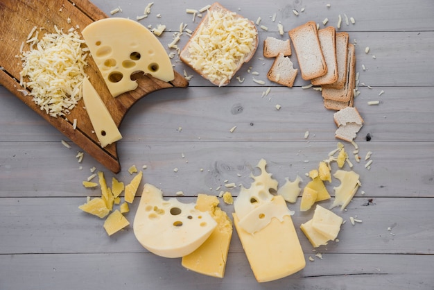 Free photo grated cheese with slices and bread on grey wooden desk