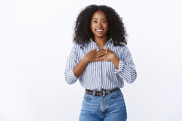 Grateful happy smiling african american girl receiving award thankful pressing palms chest grinning amazed looking appreciation delight, standing joyful amazed amused white wall