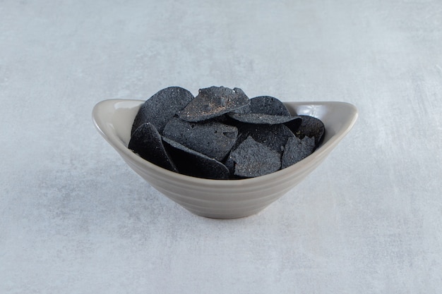 Gray bowl of crispy black chips on stone.