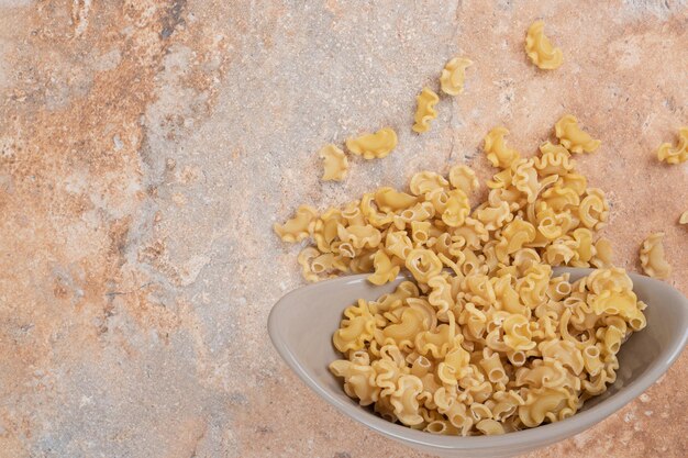 A gray bowl of unprepared macaroni on marble space. 