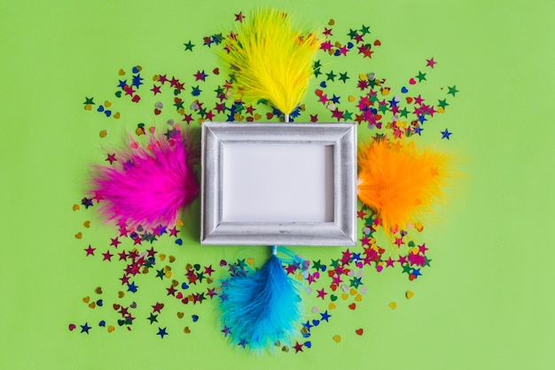 Free photo gray photo frame with confetti and colored feathers