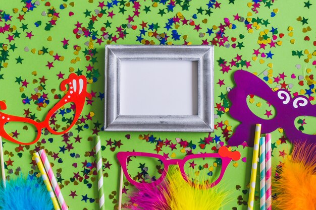 Gray photo frame with confetti, colorful glasses and sticks seen from above