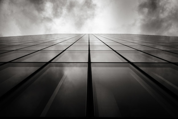 Free photo grayscale low angle shot of a skyscraper a wall with glass windows under the cloudy sky