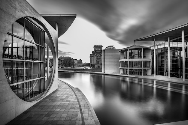 Grayscale shot of a lake in the middle of city buildings under a cloudy sky