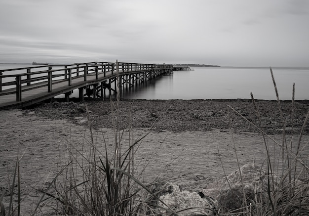 Grayscale shot of a pier on the sea surrounded by the beach under a cloudy sky