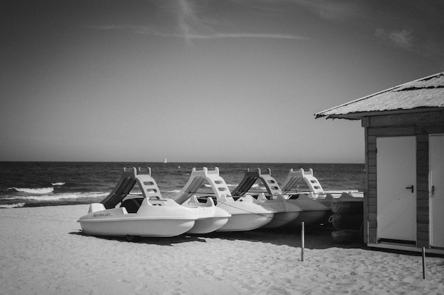 Free photo grayscale shot of watercrafts or marine vessels near a cabin on a sandy beach