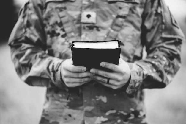 Free photo grayscale shot of a young soldier holding a bible