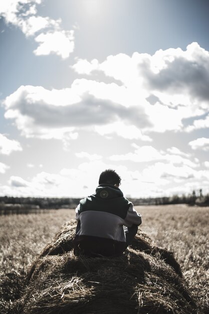 Grayscale view of man siting on hay grass