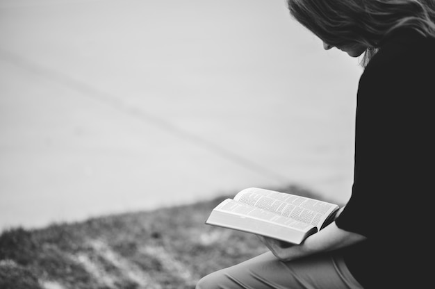 Free photo grayscale of a woman sitting outdoors while reading a book